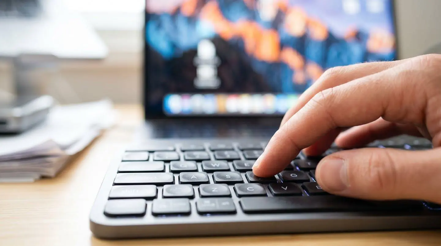 Gros plan d'une main tapant sur un clavier d'ordinateur moderne avec un écran flouté en arrière-plan