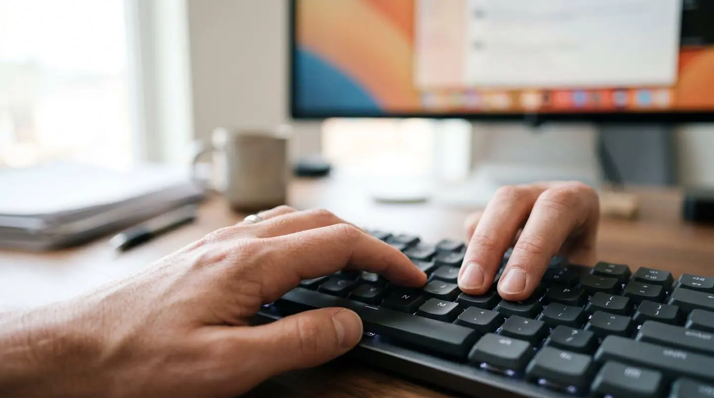 Gros plan d'une main tapant sur un clavier d'ordinateur moderne avec un écran flouté en arrière-plan