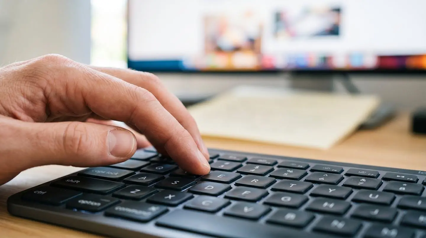 Gros plan d'une main tapant sur un clavier d'ordinateur moderne avec un écran flouté en arrière-plan