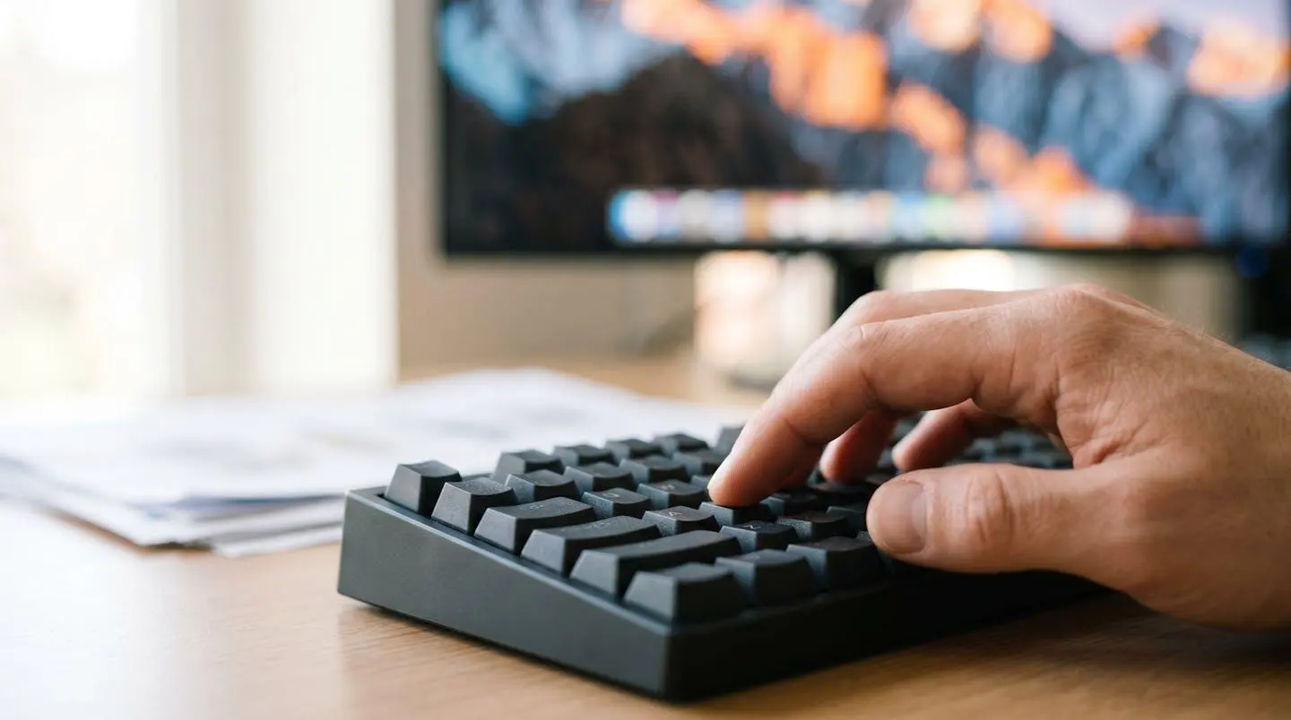 Gros plan d'une main tapant sur un clavier d'ordinateur moderne avec un écran flouté en arrière-plan